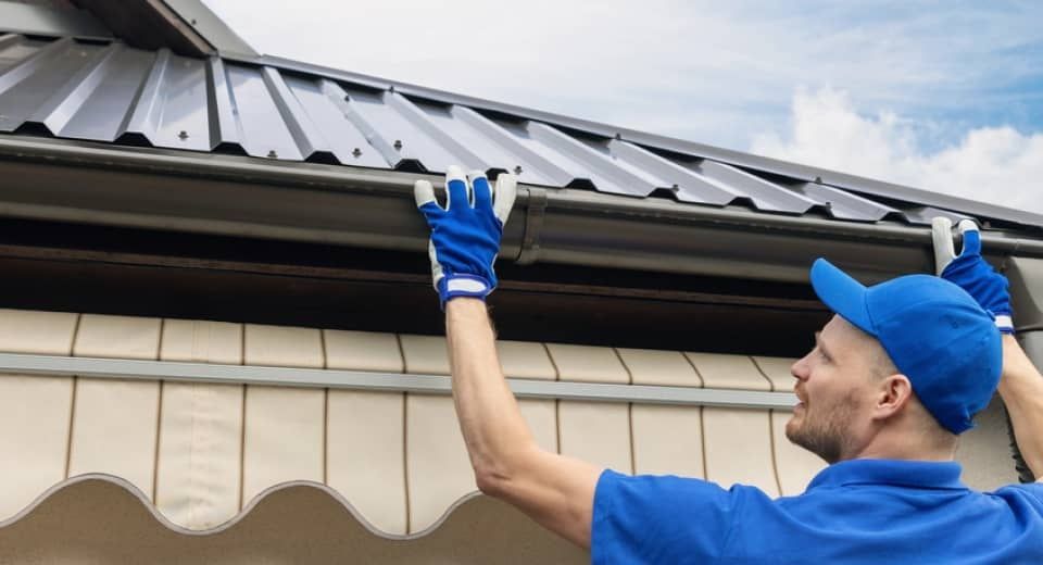 Worker in blue uniform adjusting a metal roof gutter on a house