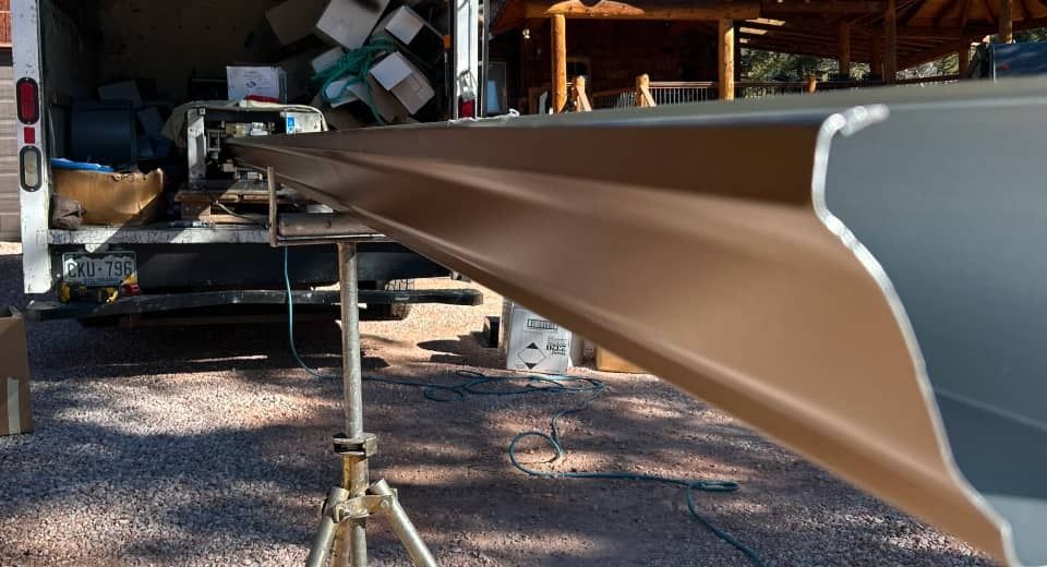 Long tan beam or rail extending from a workshop onto gravel, held by a tripod stand.