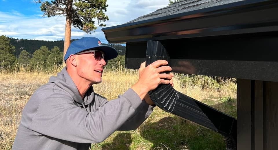 Man installing black gutter guard under roof eave on a sunny day outdoors