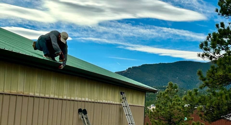 Person working on a green roof of a beige building with mountains and blue sky in the background