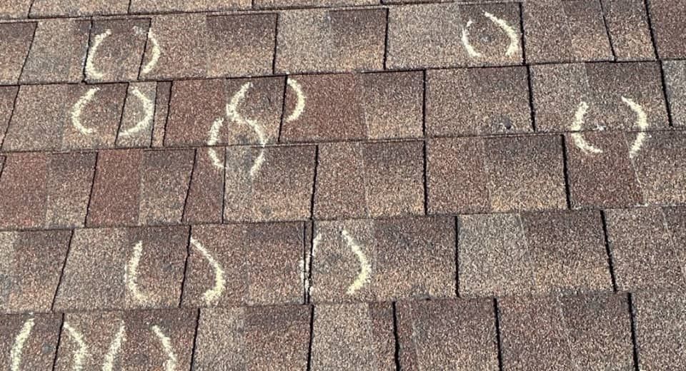 Brown roof shingles marked with white chalk circles and arrows in a repair inspection pattern