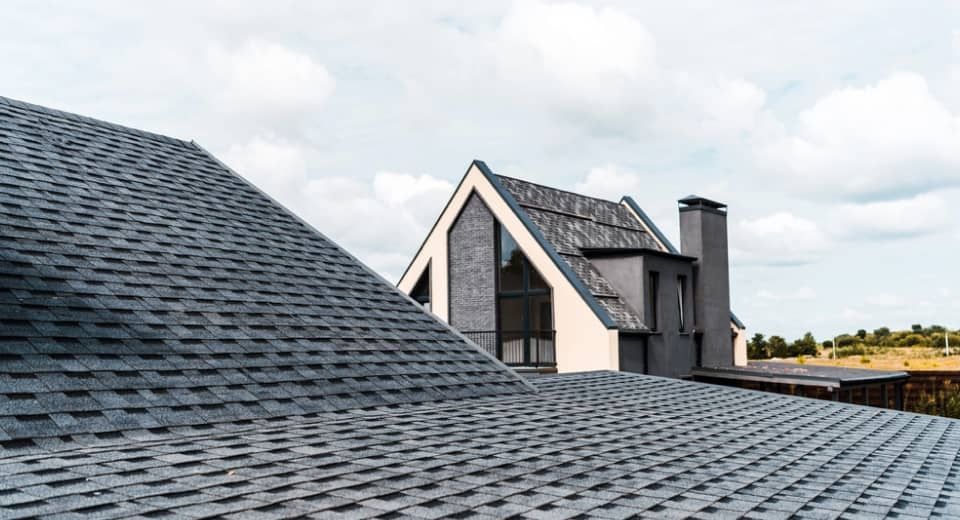 Slate roofs of modern houses under a cloudy sky, with a tall chimney and open landscape beyond