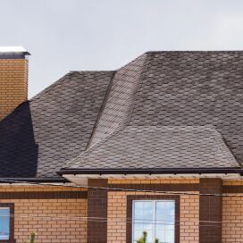 Brick house with a dark shingled roof and chimney against a pale sky