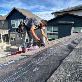 Worker on a roof using a power tool to repair shingles on a residential house.