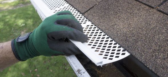 Gloved hand placing a white perforated gutter guard on a roof edge