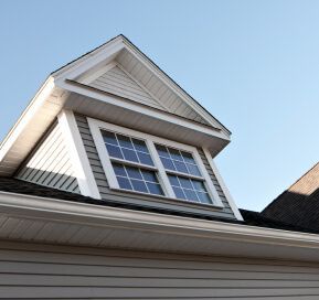 White dormer with double window on a house roof against a blue sky