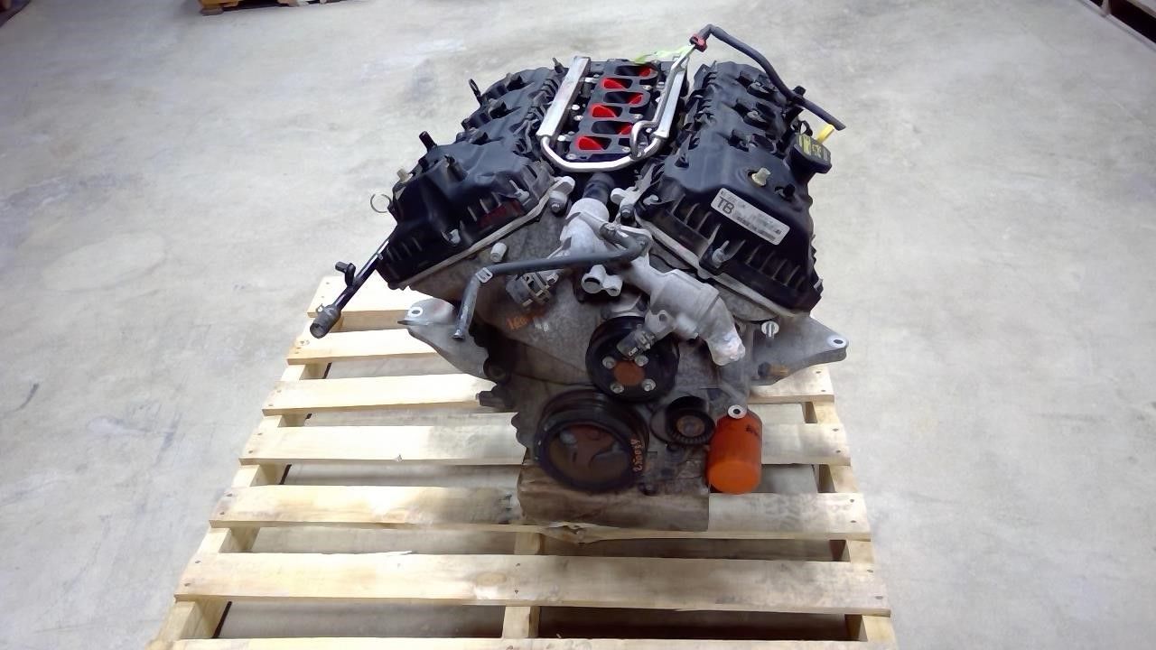 A black V8 automotive engine sitting on a wooden pallet inside a warehouse or workshop.