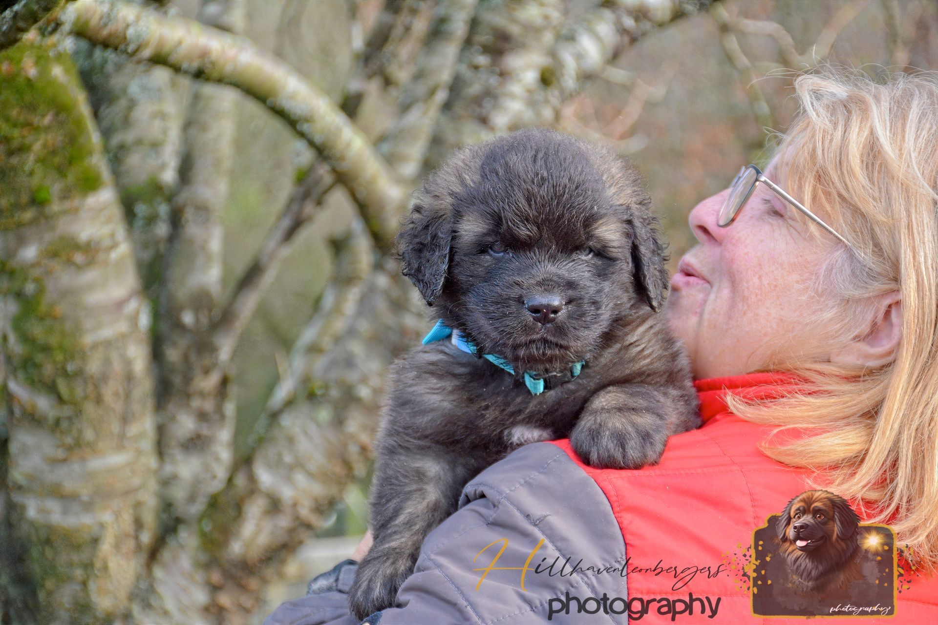 Woman holding a small black poodle outdoors, smiling as it nuzzles her face.