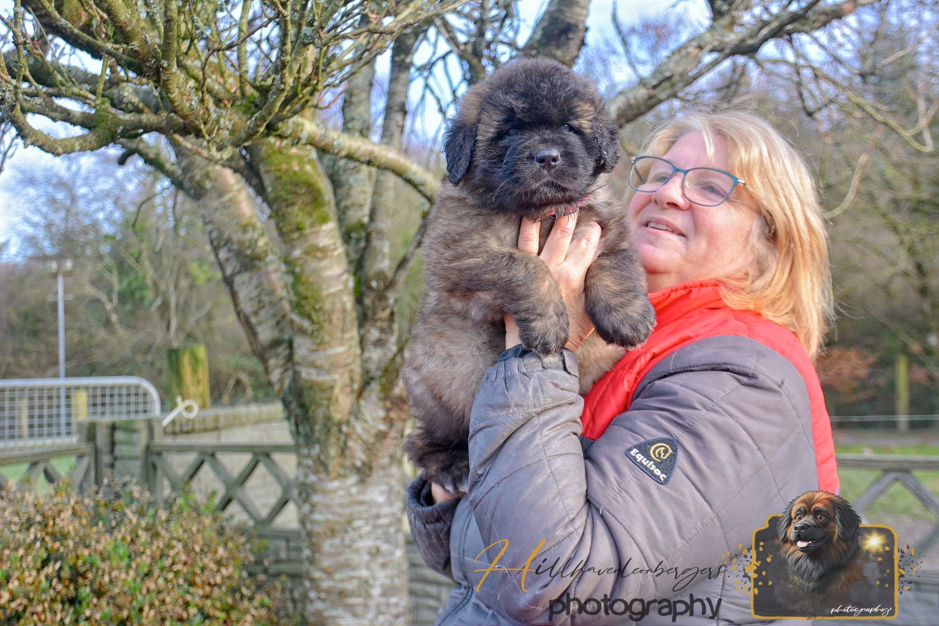 Woman holding a small black dog outdoors in a park, both facing each other.