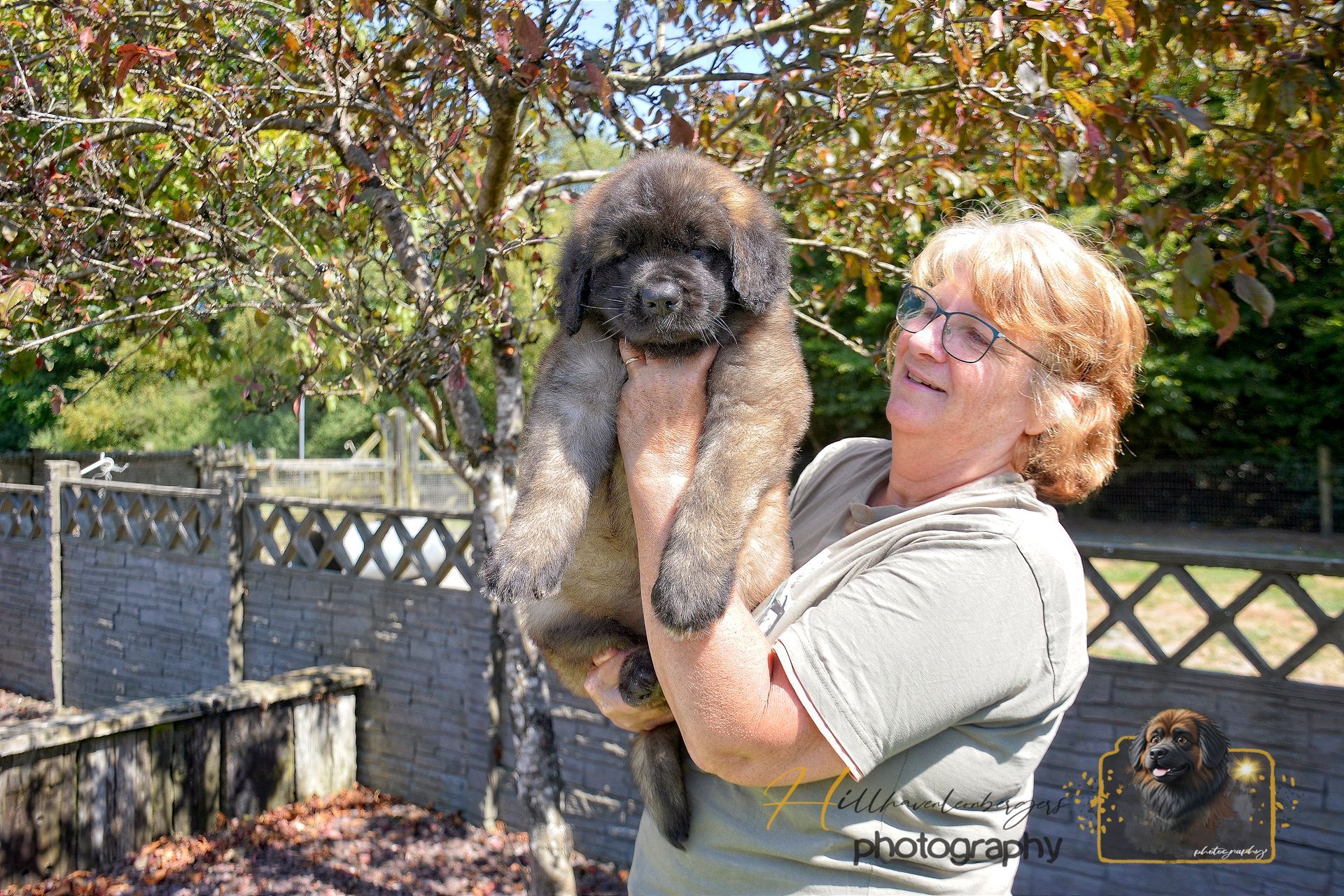 Woman holding a fluffy black-and-tan puppy outdoors in a sunny garden