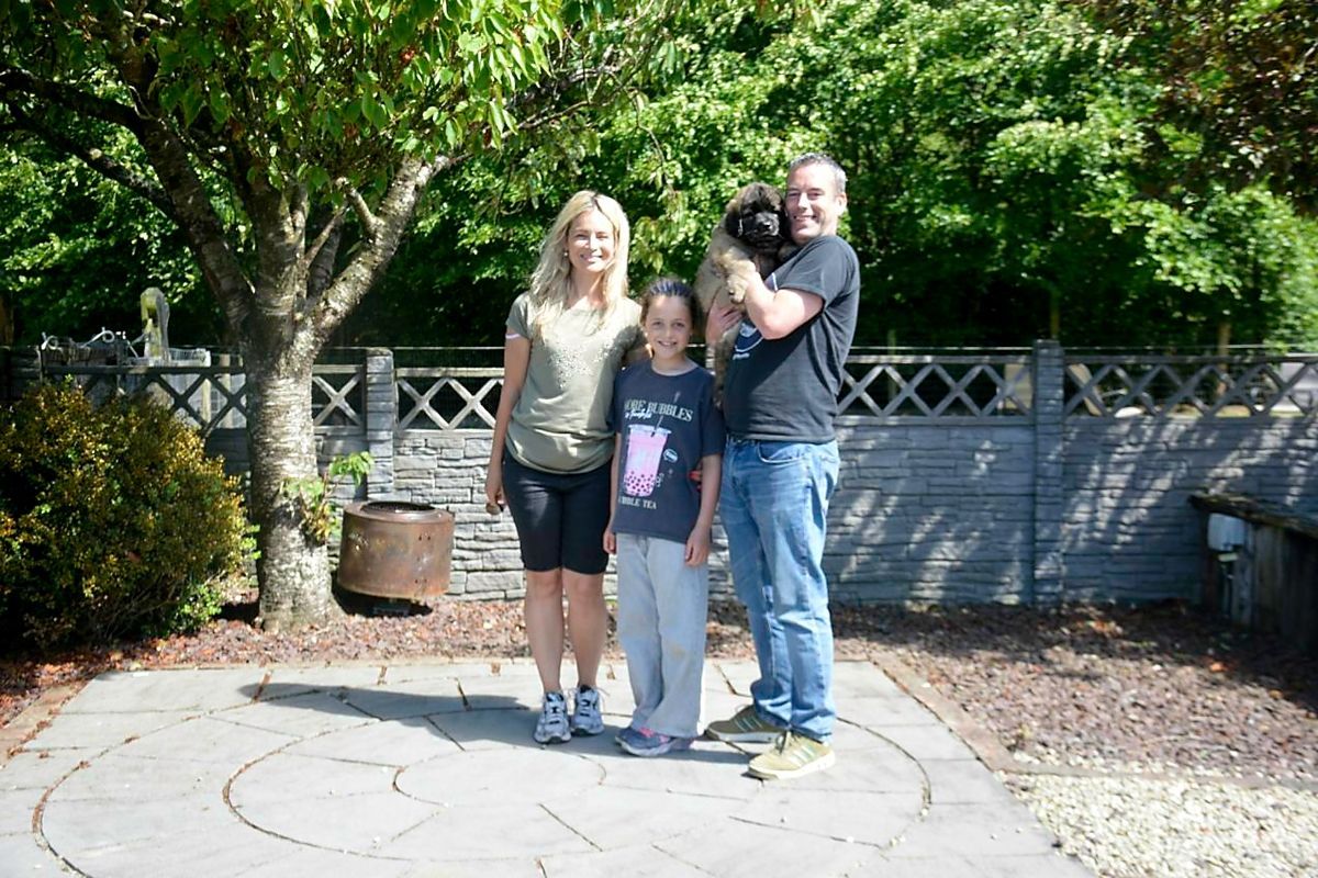 Three people standing together on a stone patio in front of a fence and trees.