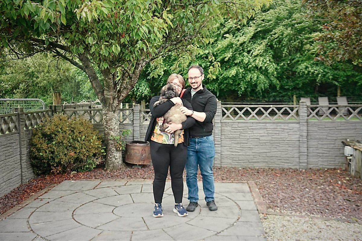 Two people hugging on a stone path in a garden with trees and a wooden fence
