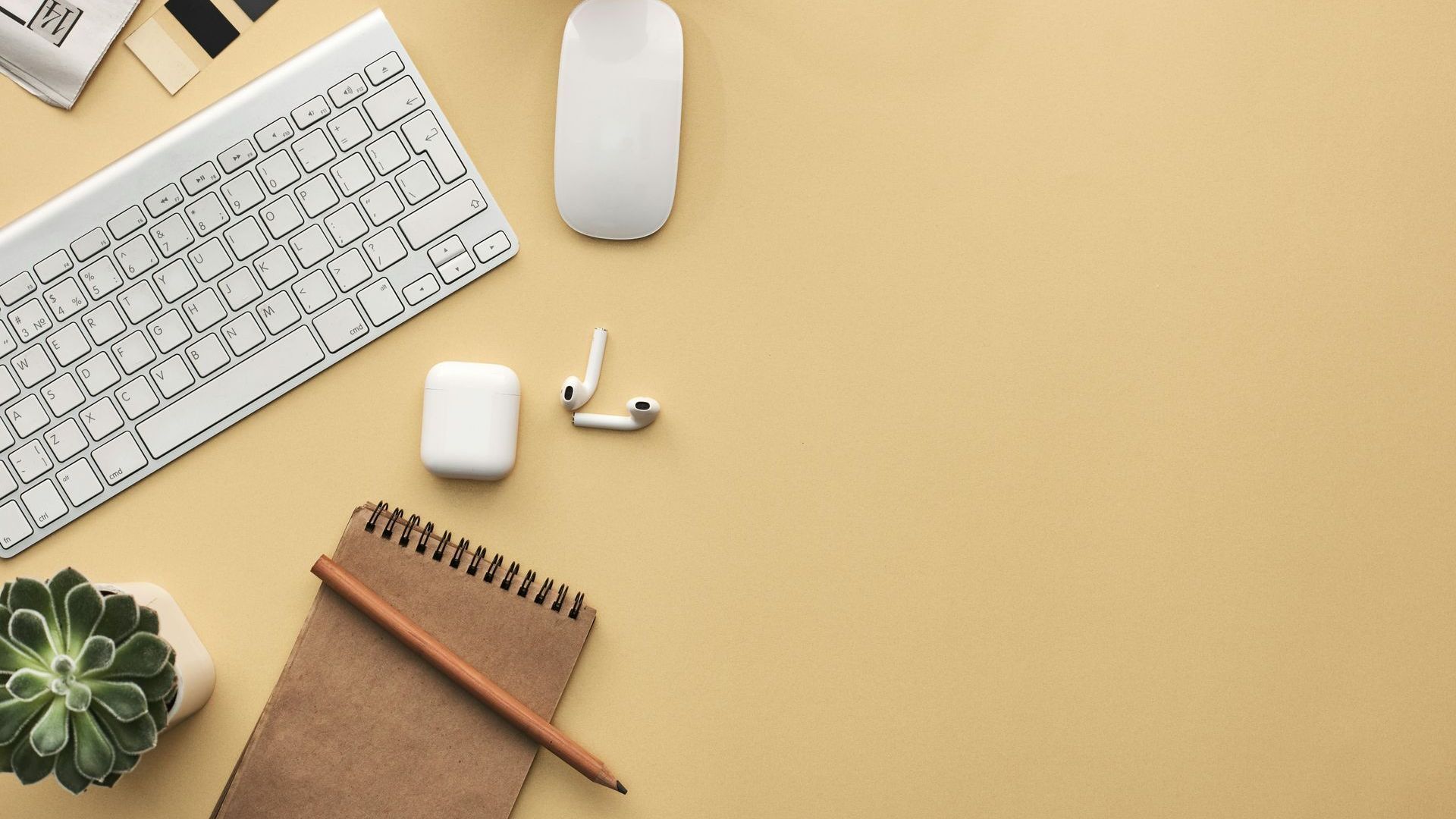 A desk with a keyboard , mouse , ear buds , a notebook , and a plant.