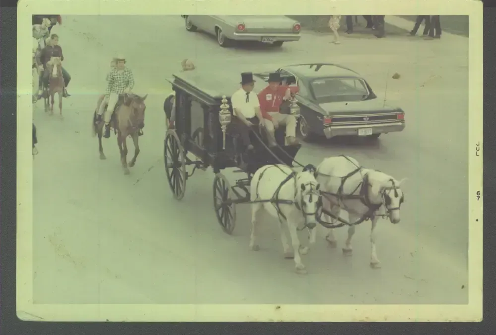 Horse-drawn carriage on a snowy street with people riding and cars passing by