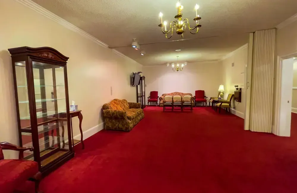 Elegant living room with red carpet, chandelier, glass cabinet, sofa, and cream curtains