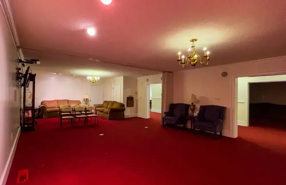 Spacious red-carpeted living room with pink ceiling, chandeliers, and seating area