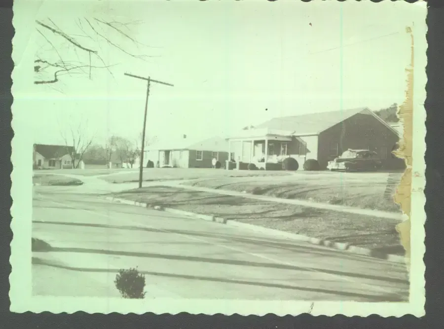 Snowy suburban street with houses, utility poles, and parked cars on a winter day