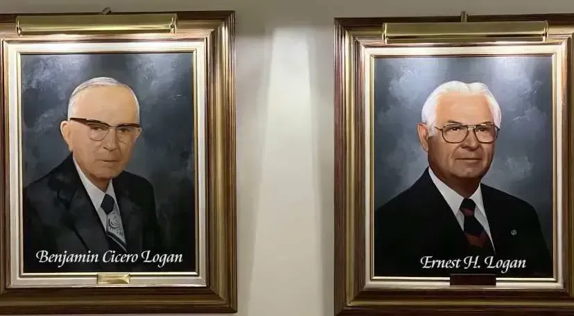 Two framed formal portraits of men with names on plaques against a wall.
