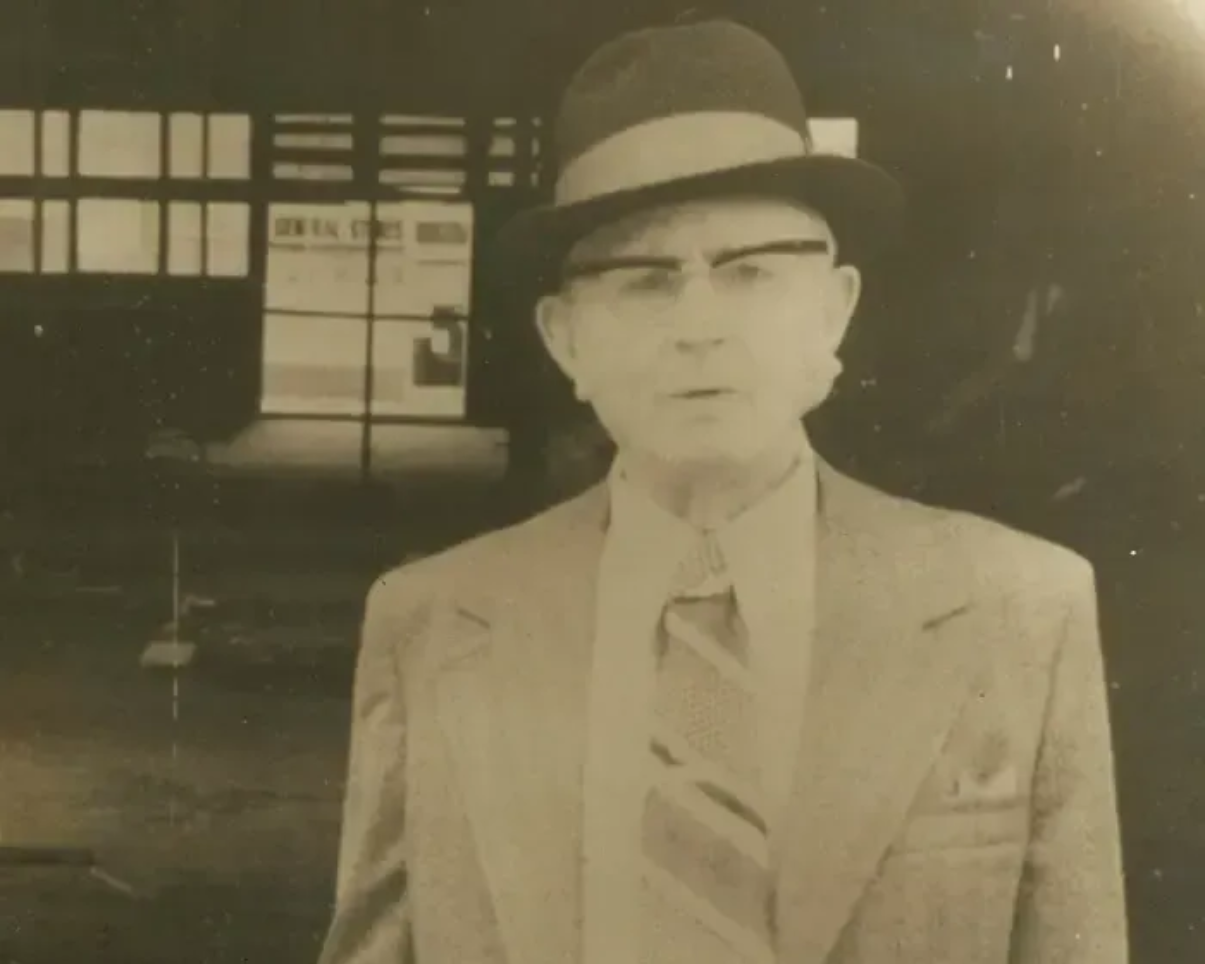 Sepia-toned portrait of a man in a suit and hat standing in front of a building