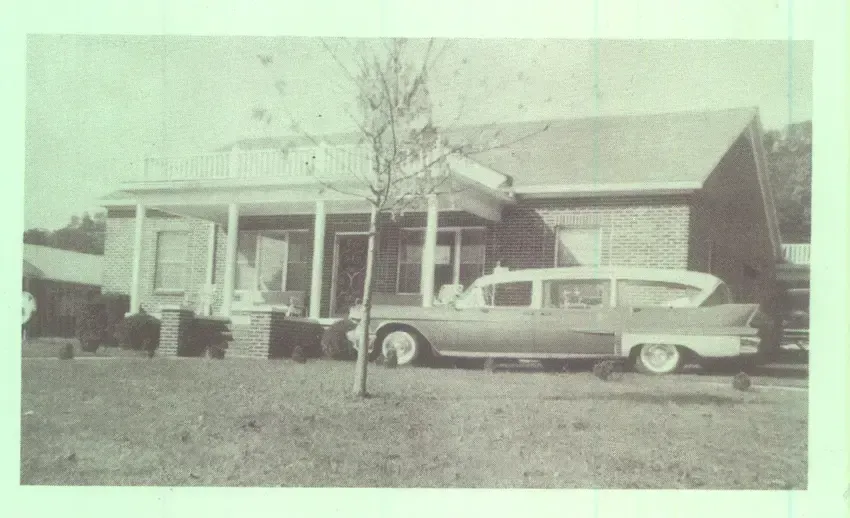 Vintage car parked in front of a small house with a porch and bare tree.