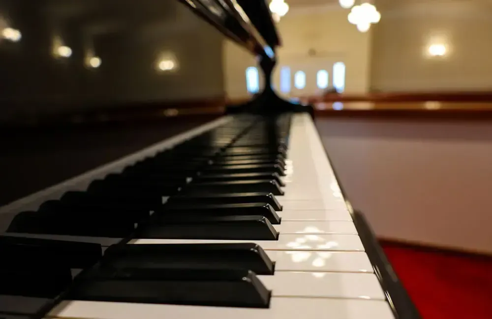 Close-up of a piano keyboard in a softly lit room, with glossy black and white keys