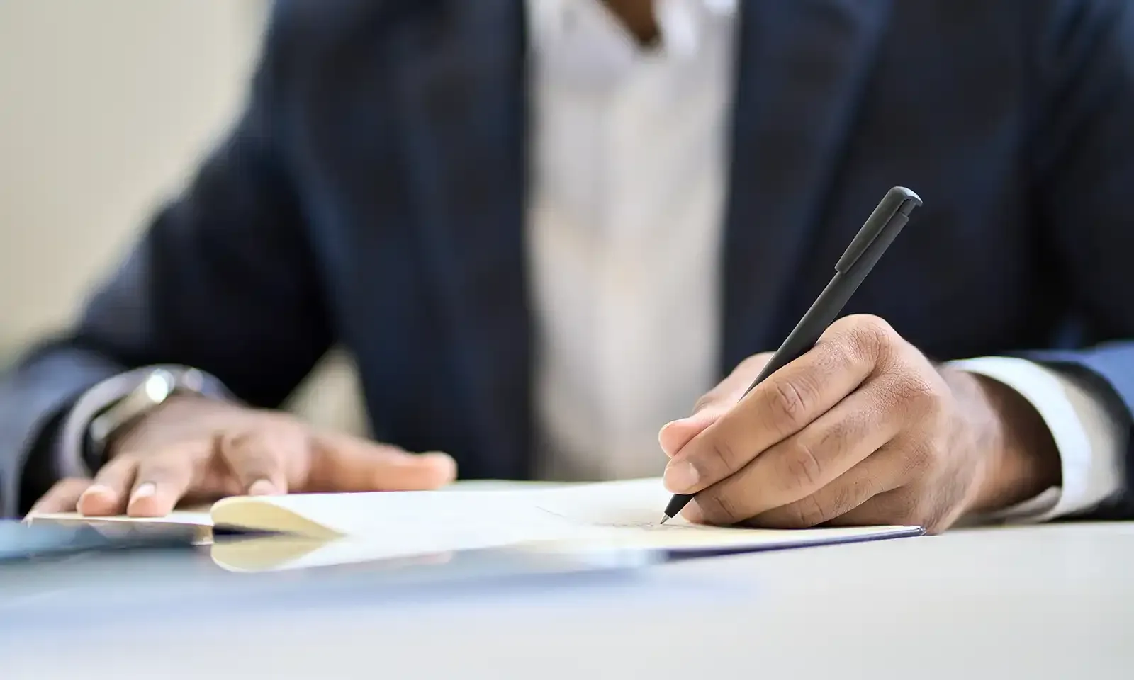 Person in a suit writing with a pen on paper, close-up shot.