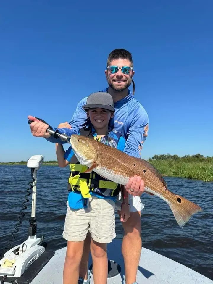 A man and a boy are standing on a boat holding a large fish.