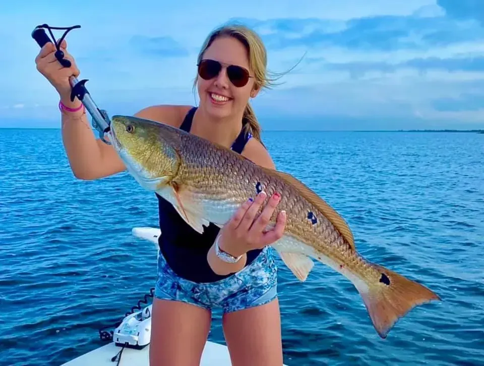 A woman is holding a large fish on a boat in the ocean.