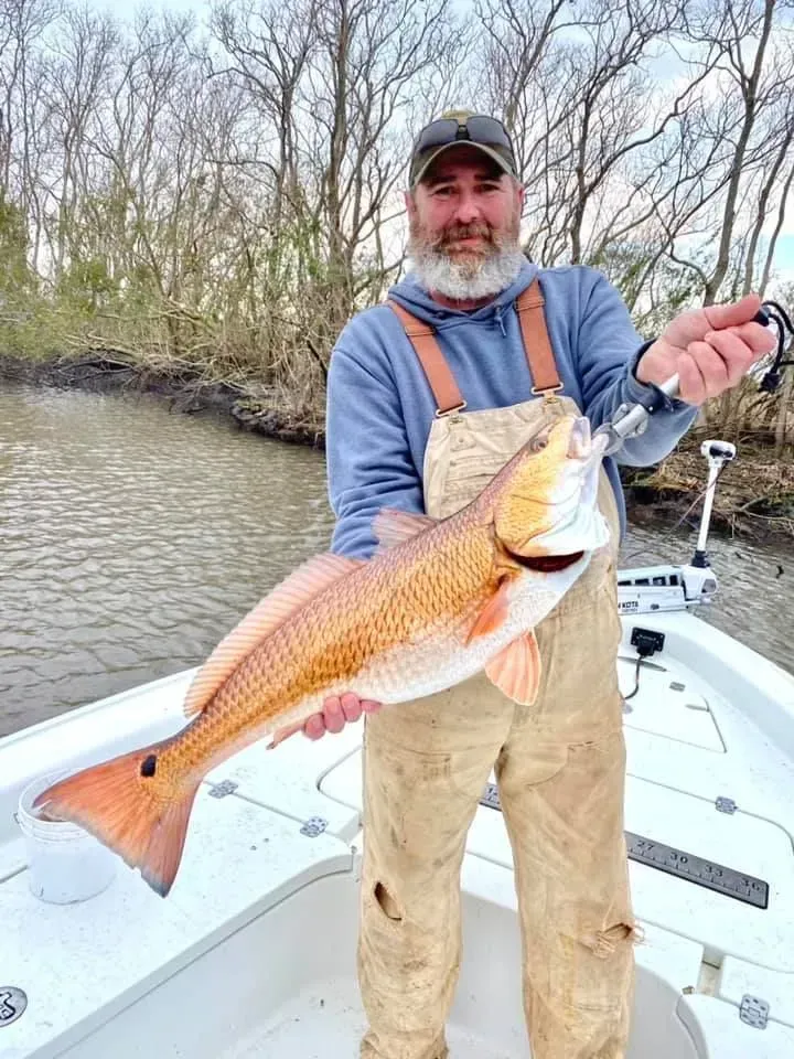 A man is standing on a boat holding a large red fish.