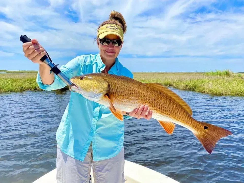 A woman is holding a large red fish on a boat.