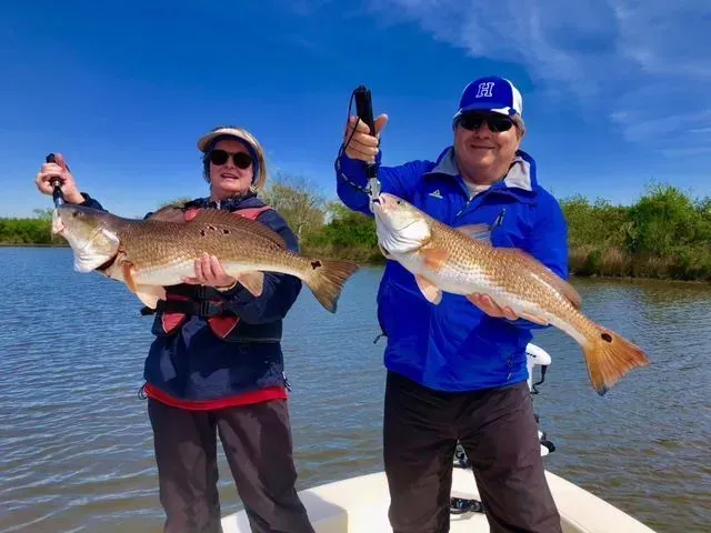 A couple is standing on a boat holding two large fish