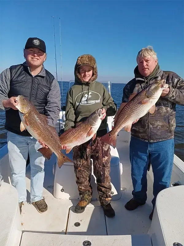 Three men are standing on a boat holding fish.