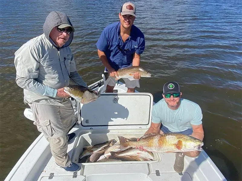 Three men are sitting on a boat holding fish.