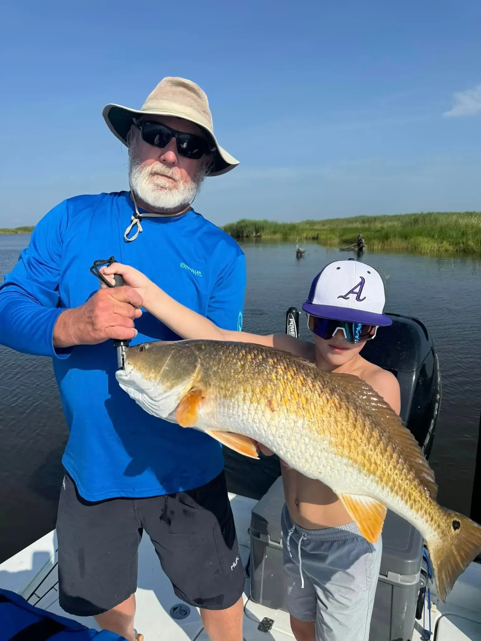 A man and a boy are holding a large fish on a boat.