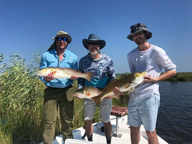 Three men are standing on a boat holding large fish.