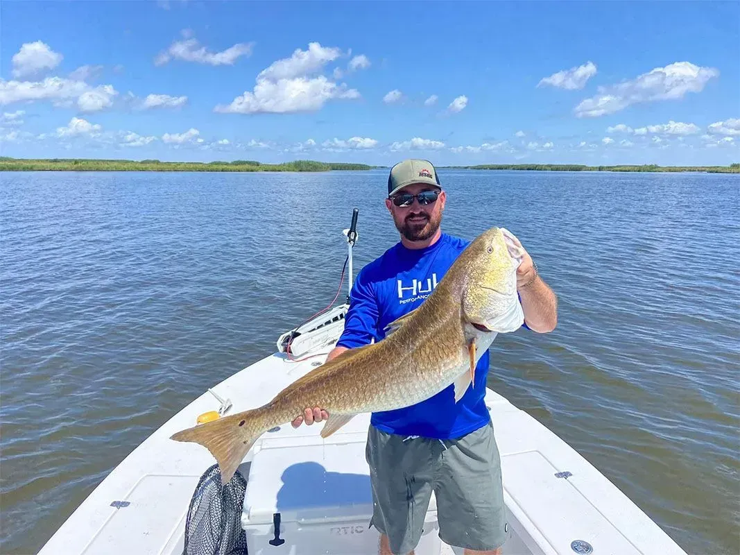A man is standing on a boat holding a large fish.