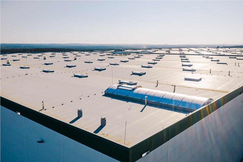 Aerial view of a large warehouse roof, with many vents and skylights under a sunny sky.