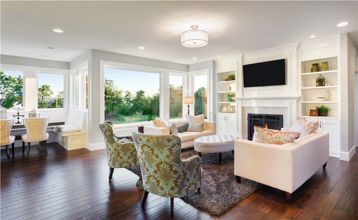 Spacious living room with hardwood floors, white walls, and large windows overlooking greenery