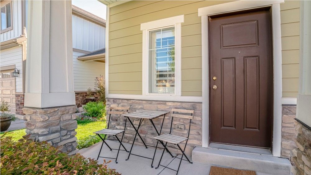 Exterior of a home with a brown door, small bistro table, and a stone accent wall; green siding.