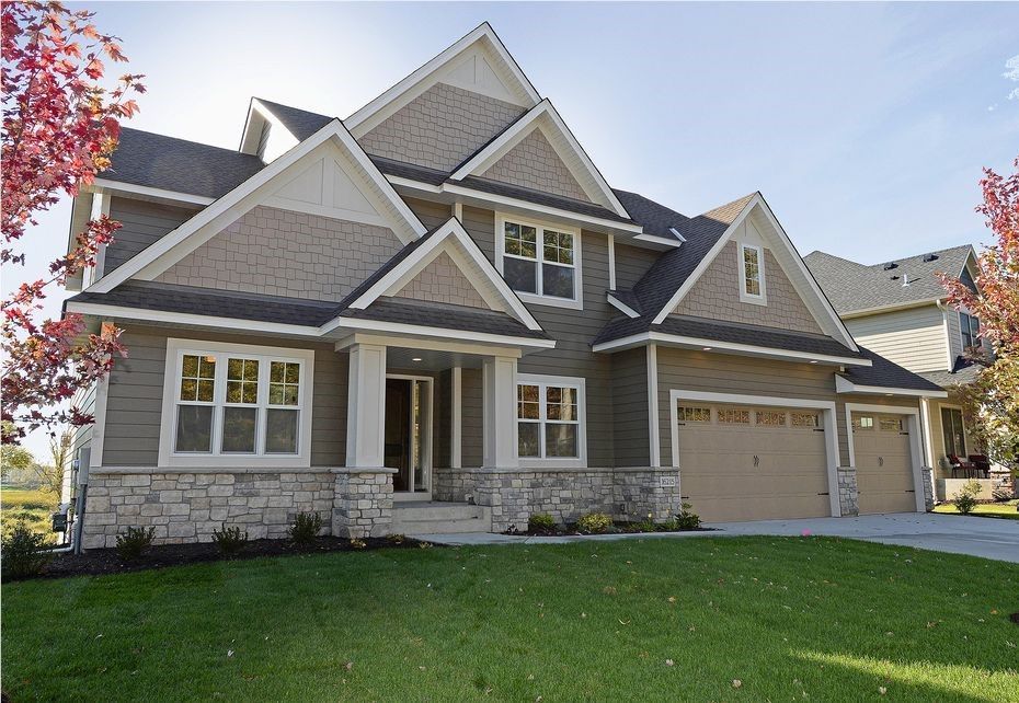 A two-story house with a green lawn, stone accents, and beige siding under a blue sky.