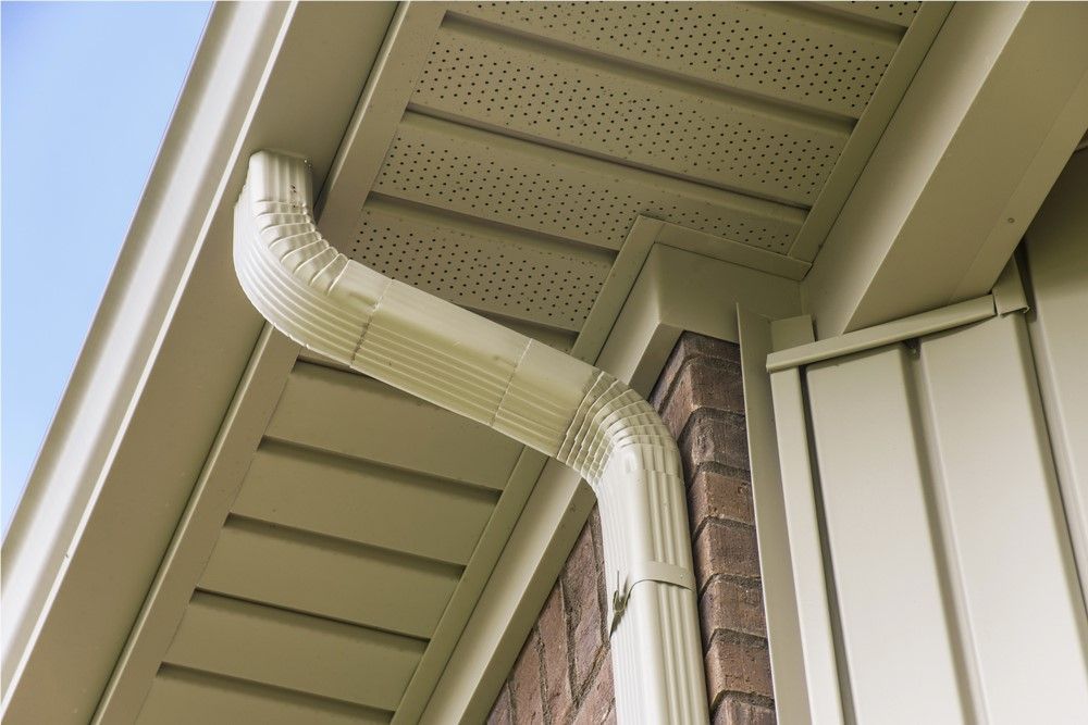 Beige guttering on a house, diverting rainwater. The corner of the house shows brick and siding.