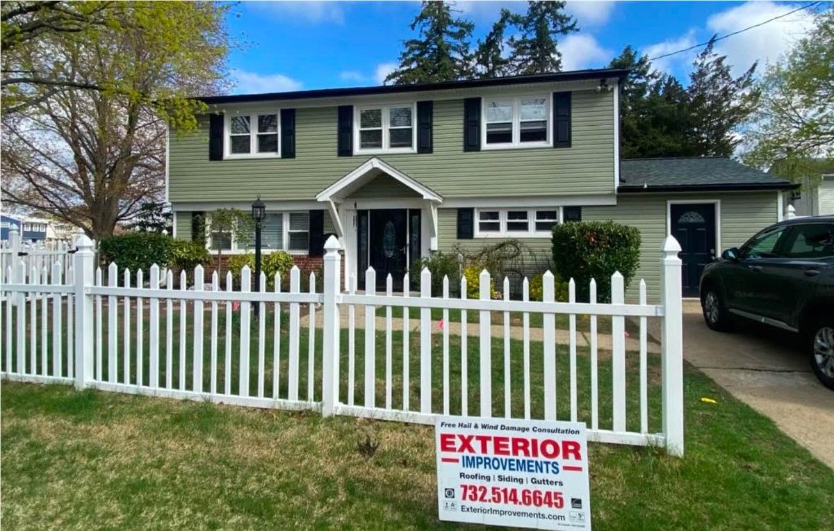 Two-story house with a white picket fence. The house is light green with black shutters