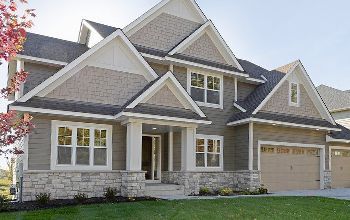 Two-story house with a stone facade, beige siding, and a tan garage door. The house has a gabled roof and multiple windows.