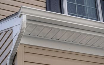 White gutters and siding of a house, close-up with a window and dark shutter visible above.