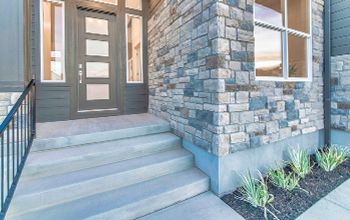 A stone-clad house entryway with concrete steps and a dark gray door with glass panels.