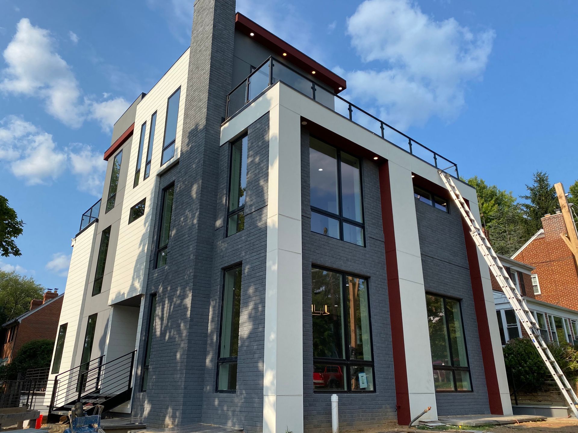 Modern multi-story home with gray and white siding, a rooftop deck, and a tall chimney under a blue sky.