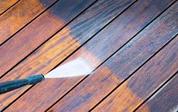 Pressure washing a wooden deck, revealing the cleaned, lighter color.