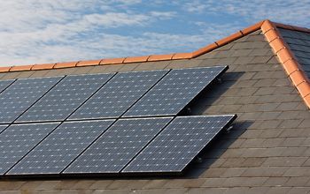 Solar panels installed on a slate roof with orange trim and a blue sky background.