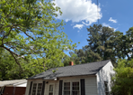 Small white house under leafy green trees with a blue sky and clouds above