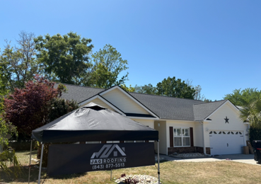 House with a black dumpster and roof replacement tent in the driveway on a sunny day